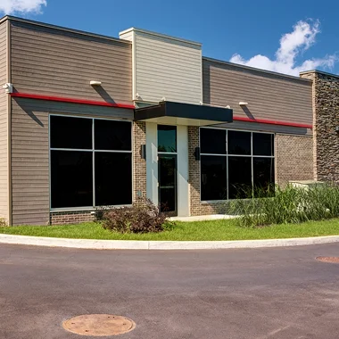 Single story commercial building with large front windows and a clean modern exterior under a blue sky. The image supports the section about improving energy efficiency, privacy, and comfort in commercial spaces with window tint.