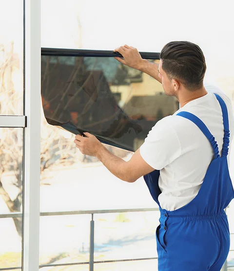 Technician installing window film on a large commercial window by carefully applying and smoothing the tint sheet onto the glass. The image supports the section about professional commercial tint installation for reducing heat, glare, and UV exposure.
