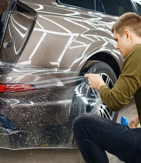echnician carefully installing paint protection film along the side panel of a vehicle, stretching and aligning the film over the wheel area. The image supports the section about shielding vulnerable areas from damage while maintaining a clean factory finish.