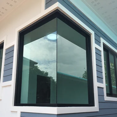 Modern home exterior with large corner windows reflecting the sky and surrounding neighborhood. The image supports the section about residential window tint improving energy efficiency, reducing heat, and maintaining a clean appearance.