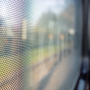 Close up of perforated window film applied to glass creating a blurred view while still allowing light to pass through. The image supports the section about added privacy and reinforced glass surfaces with security window film.